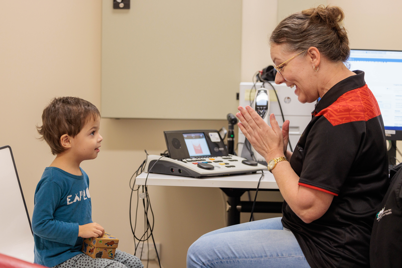 An audiologist, smiling and clapping her hands while interacting with an Indigenous child at a ear health for Mob appointment.