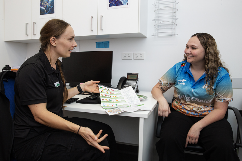A dietitian sitting with an Indigenous client in the clinic, having a yarn about diets using a infographic brochure.