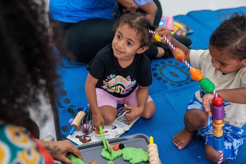 A playgroup with two young Indigenous children playing with playdough and a rope with giant beads on it, supporting Indigenous child health in Goodna.