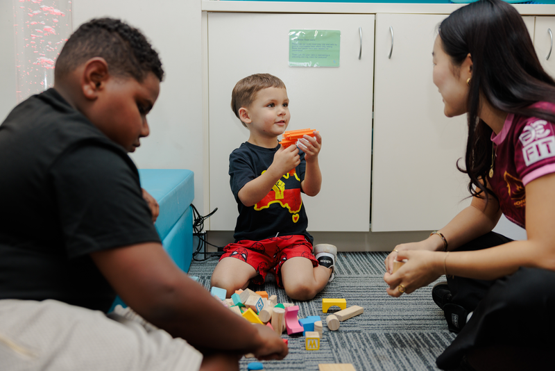 Two children sit with a worker playing with building blocks on the carpet for occupational therapy for Mob.